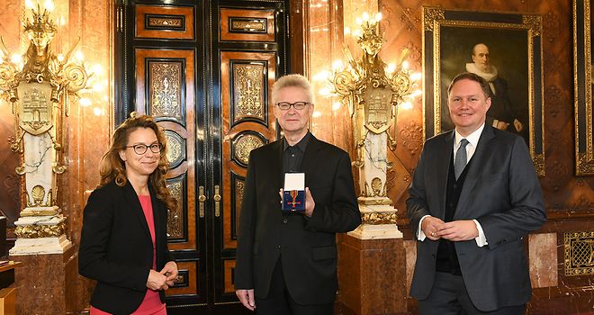Carola Veit, Michael Batz und Dr. Carsten Brosda posieren nebeneinander für ein Foto. Michael Batz präsentiert den Bundesverdienstorden