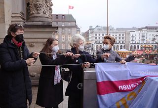 Veit, Leonhard und die beiden Vertreterinnen von „Terre des Femmes" stehen auf dem Rathausbalkon und ziehen an der Kordel zum Hissen der Flagge.