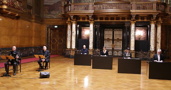 Die Sprecherinnen und Sprecher sowie zwei Musikanten sitzen im Großen Festsaal und führen die szenische Lesung auf.