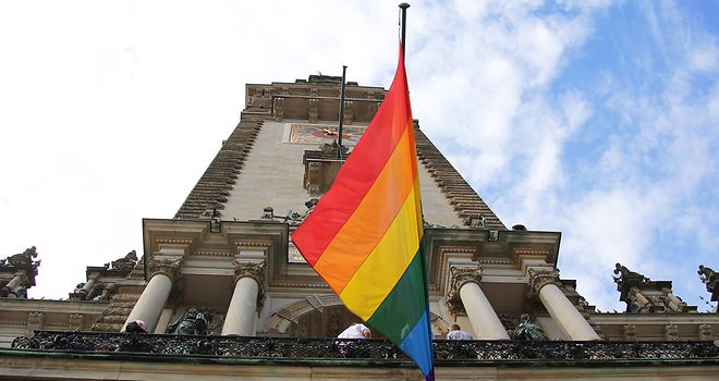 Blick von unten nach oben zum Rathausturm an dem die Regenbogenflagge weht.