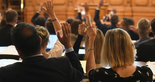 Die Abgeordneten sind von hinten zu sehen, wie sie bei einer Bürgerschaftssitzung zur Abstimmung die Hände heben.