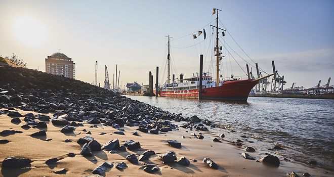 Morgendlicher Elbstrand mit Steinen im Vordergrund, Segelschiff schwimmt auf dem Wasser
