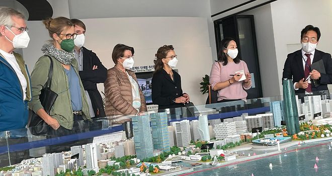Gruppe Menschen steht hinter einem Miniaturmodell von Busans Skyline und lauscht den Ausführungen eines Erklärers.
