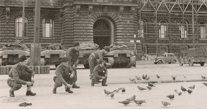 Mehrere britische Soldaten füttern Tauben vor dem Hamburger Rathaus. Im Hintergrund stehen Panzer.