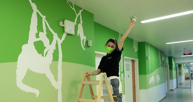 Eine Malerin vor der neuen Flurgestaltung im Kinder-UKE. Die Wände zeigen Tiermotive auf grünem Hintergrund.