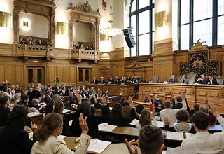 Blick in den Plenarsaal, in dem eine Bürgerschaftssitzung stattfindet. Die Abgeordneten heben zur Abstimmung die Hand.