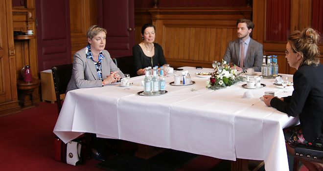 Alda Vanaga, Carola Veit und weitere Personen sitzen im Gespräch an einem Tisch.