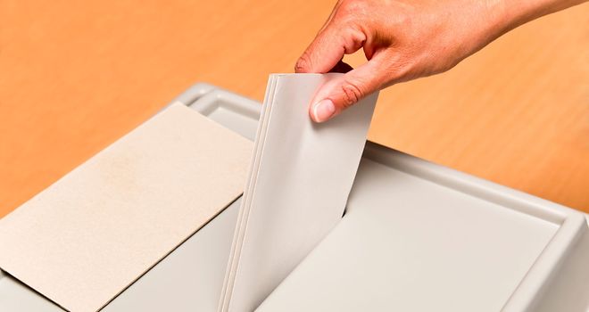 Eine Hand steckt einen Wahlzettel in eine Wahlurne