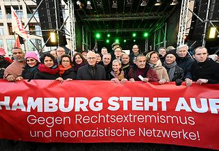 Viele Personen halten ein großen roten Banner in den Händen mit der Aufschrift „Hamburg steht auf. Gegen Rechtsextremismus und neonazistische Netzwerke!"
