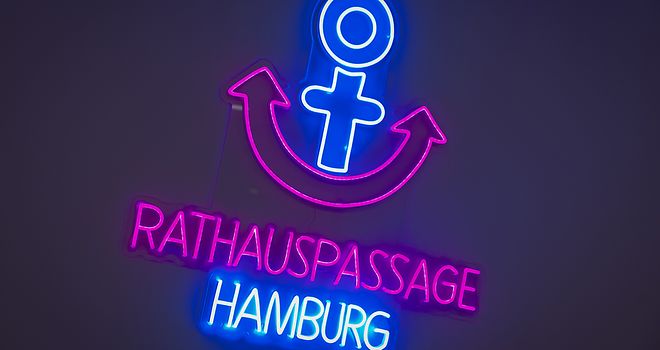 Es ist das beleuchtete Logo der Rathauspassage Hamburg zu sehen.