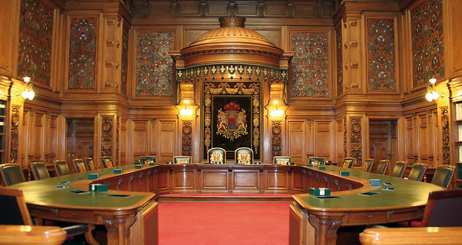 Die Ratsstube wird eingenommen von einem hufeisenförmigen Tisch, um den herum ledergepolsterte, genagelte Stühle mit Armlehnen angeordnet sind.