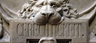 Baudetail eines Reliefes am Hamburger Rathaus. Es zeigt einen Löwenkopf mit dem Wort Gerechtigkeit im Maul.
