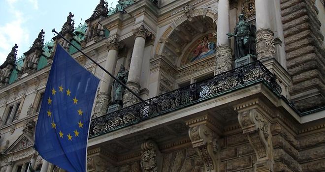 Blick von unten nach oben zum Rathausbalkon an dem die Flagge der EU und die Hamburger Flagge wehen.